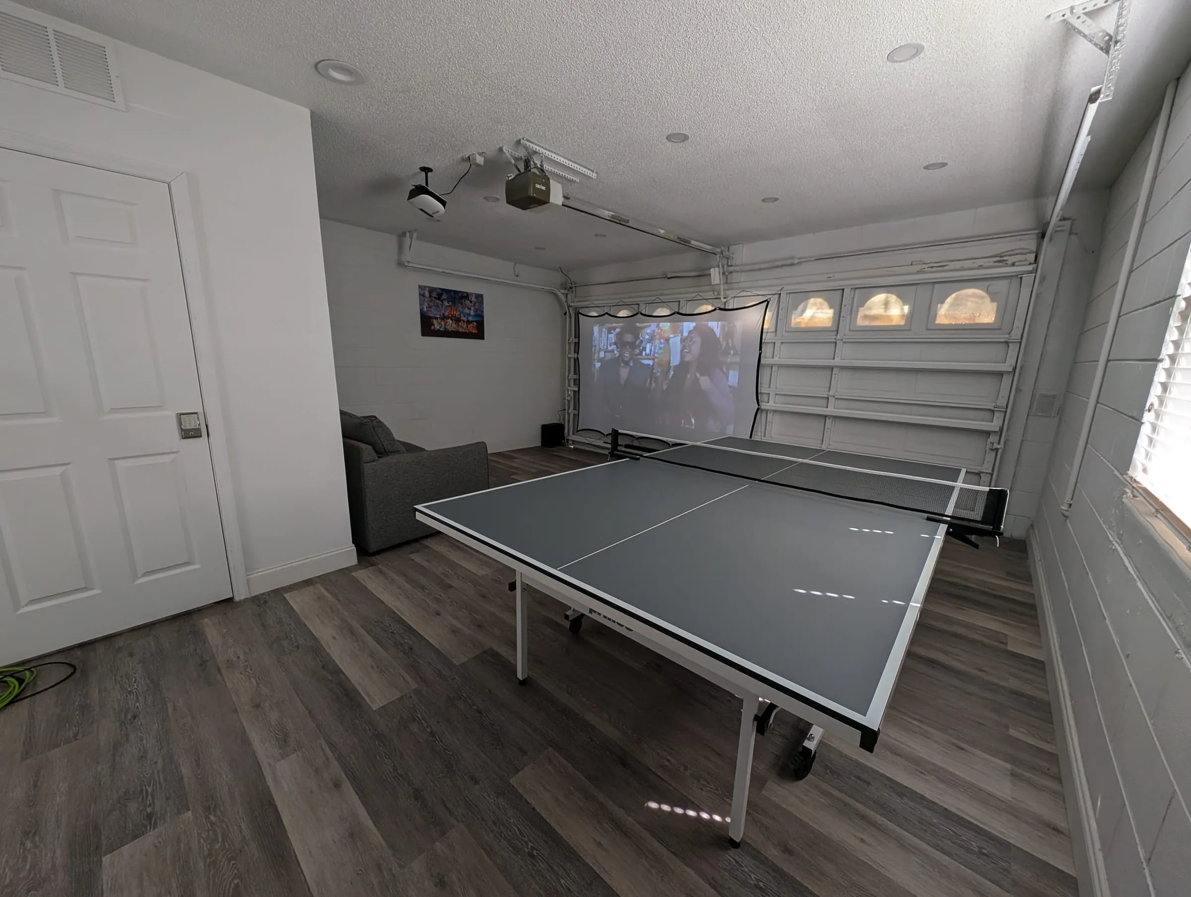 Wide view of the theater room showing the projector screen, ping-pong table, and sofa